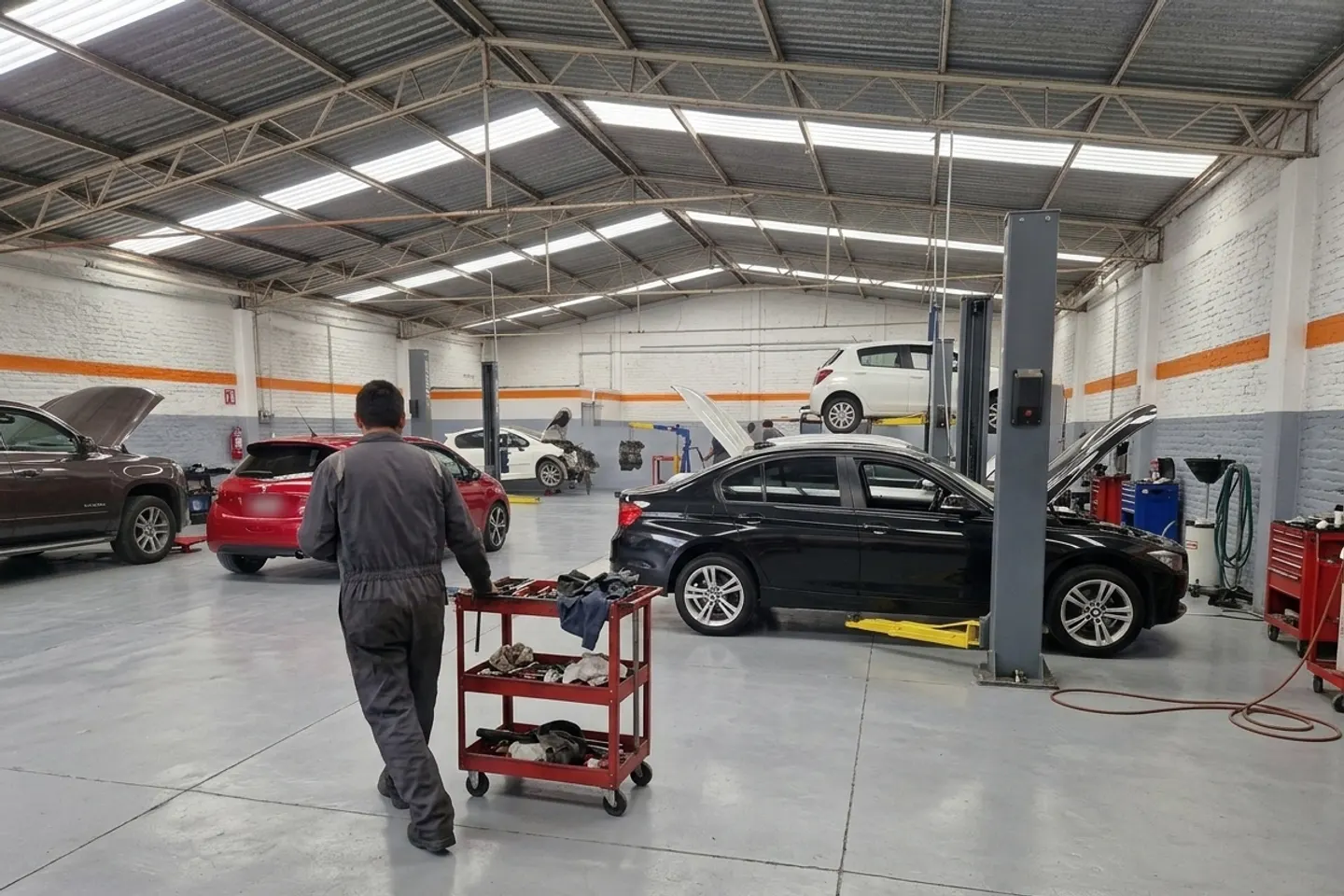 Mecánico con un carrito de herramientas en un taller con autos europeos en servicio