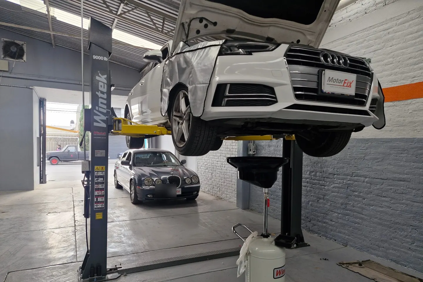 Audi A4 blanco sobre un elevador durante un cambio de aceite en el taller Motorfix