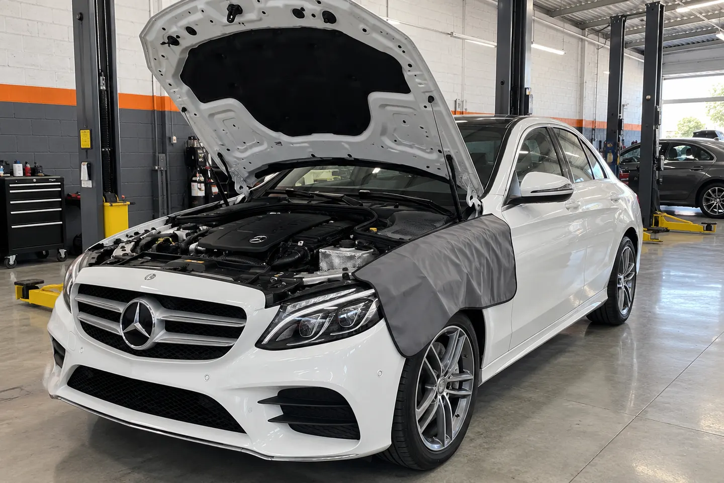 Mercedes-Benz Clase C blanco con el cofre abierto y funda protectora en un taller