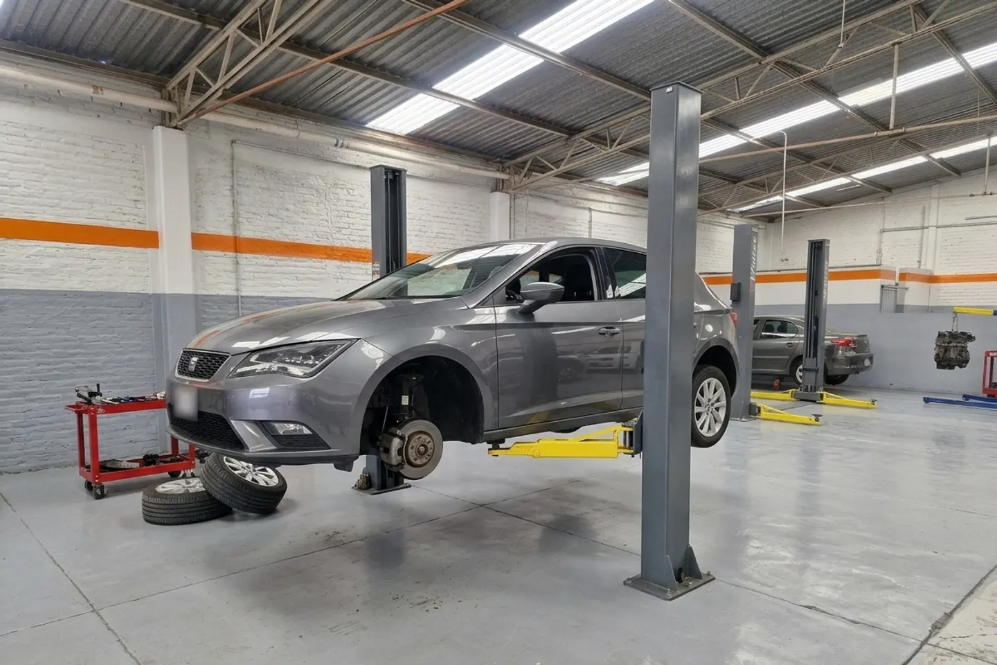 Seat León gris sobre un elevador, con una rueda desmontada, en un taller