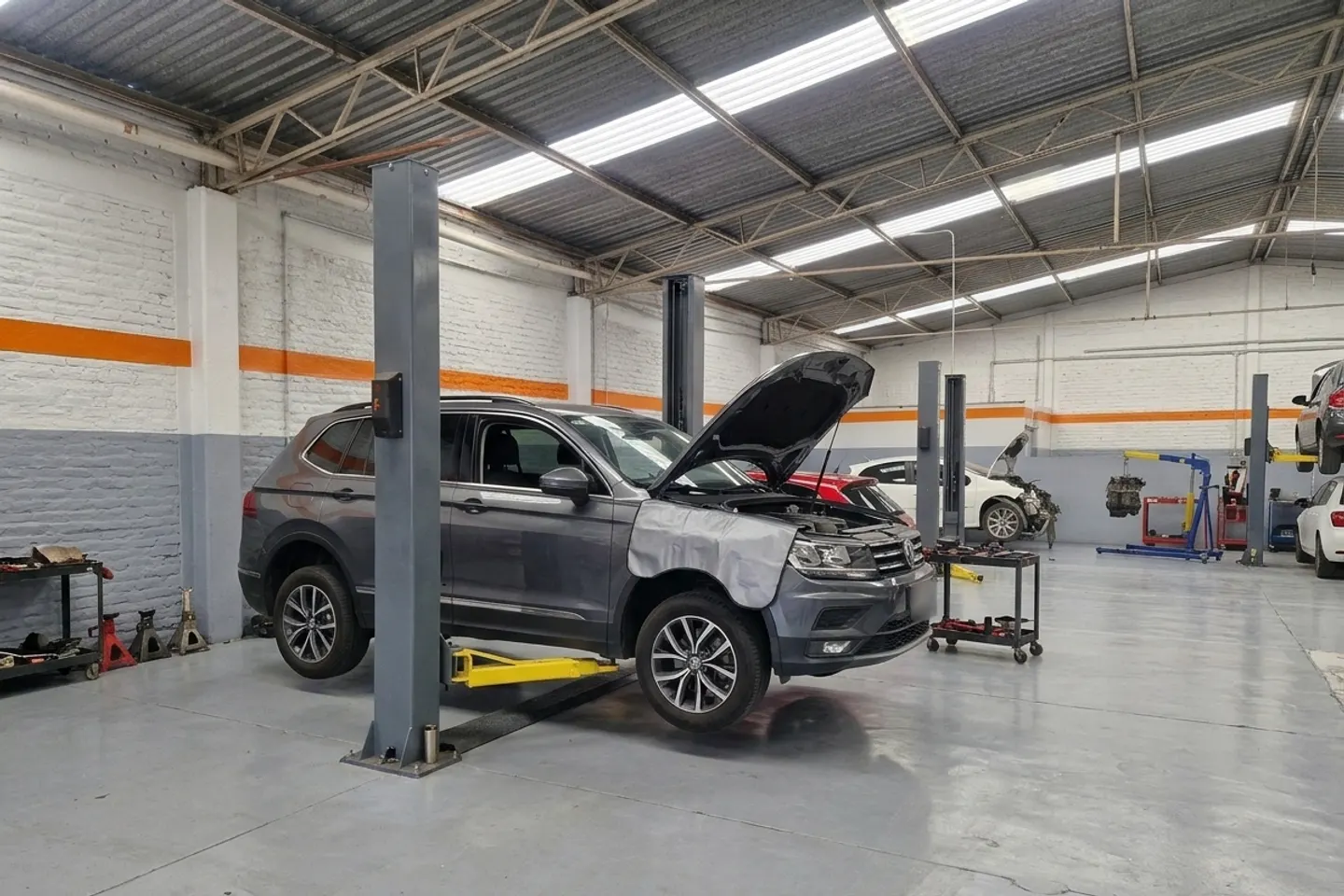 Volkswagen Tiguan gris con el cofre abierto sobre un elevador en un taller
