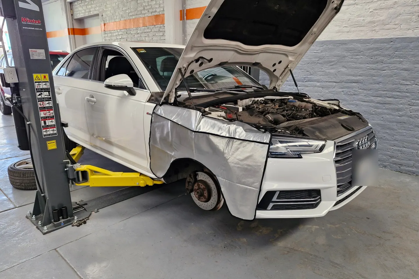 Audi A4 blanco sobre un elevador con la rueda desmontada y el disco de freno a la vista, en el taller Motorfix