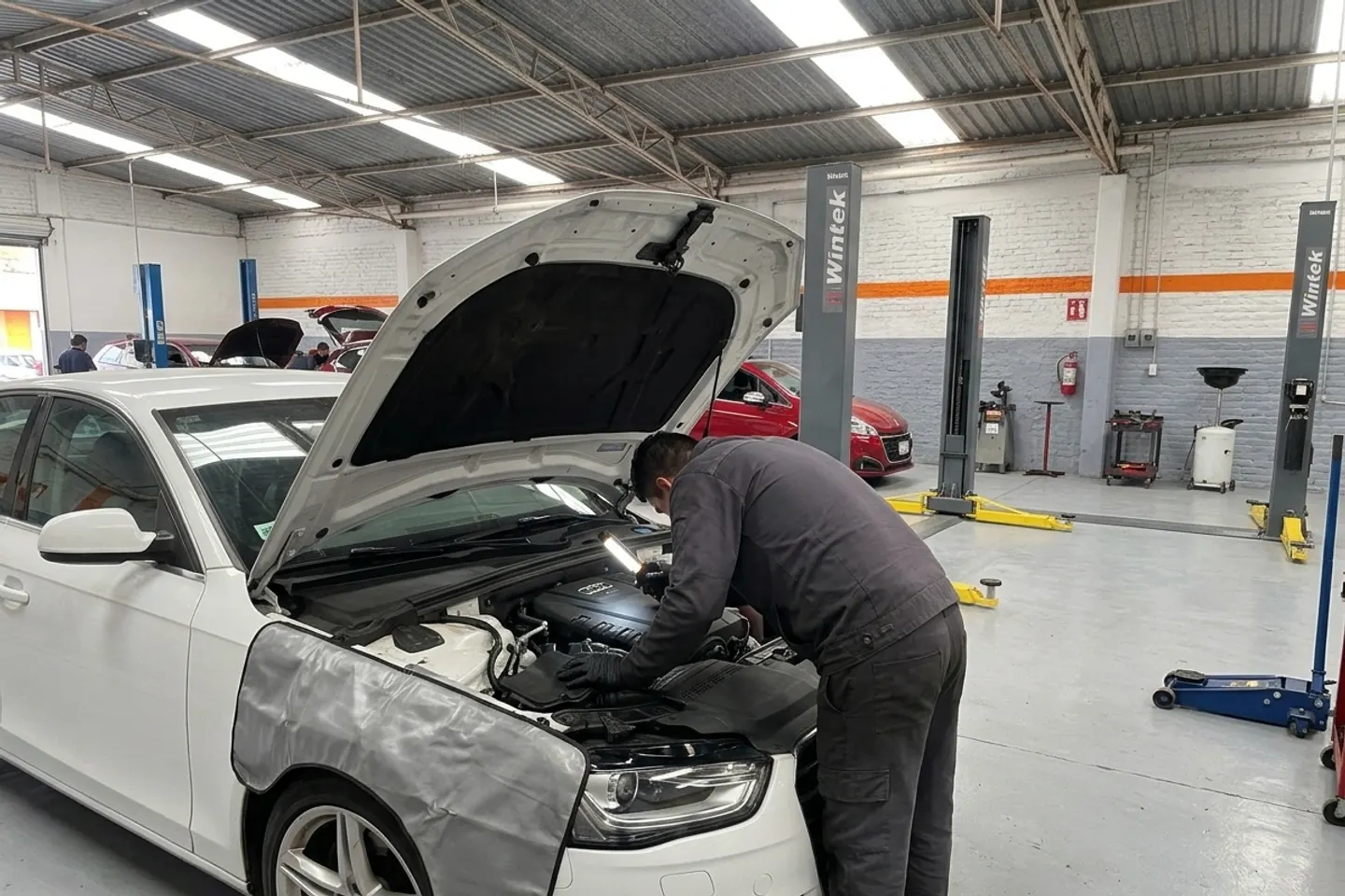 Mecánico revisando el motor de un Audi blanco con el cofre abierto